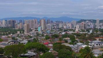 Aerial view of Honolulu, Hawaii, featuring high rise buildings, residential areas, open green spaces, and distant mountains with slow motion pan. video