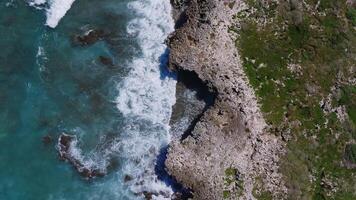 Aerial view of Oahu's rocky coastline with turquoise waves crashing against the shore. A person stands near a pathway, adding scale to the scene. video