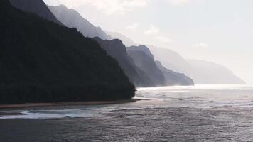 Aerial view of the Napali Coast on Kauai Island, Hawaii, with jagged cliffs, rolling ocean waves, and light and shadow across the rugged terrain. video