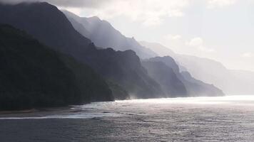 Serene aerial view of Napali Coast on Kauai Island, Hawaii, with rugged cliffs, sunlight, mist, and a slow pan along the coastline over the ocean. video
