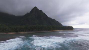 Aerial view of Kauai's Napali cliffs with waves crashing against the shore, turquoise ocean, dense greenery, and low hanging clouds. video
