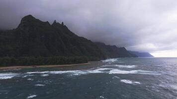 Aerial view of the Napali Coast on Kauai Island, Hawaii, with rugged cliffs, lush greenery, ocean waves, and an overcast sky in a slow flyover motion. video