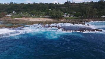 Aerial view of Oahu's rocky coastline with waves crashing against dark rocks. Turquoise waters and greenery create a dynamic natural scene. video