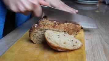 A girl slices bread with a large knife on a wooden board. Cooking, table setting video