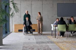 A diverse team of business colleagues, including a director in a wheelchair, engages in a collaborative discussion as they move together through a modern office space photo