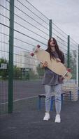 Girl standing in front of a net with a longboard in her hands, vertical video