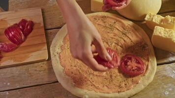 Baker carefully laid out thinly sliced tomato slices on top of pizza base, which was made from raw dough and covered with tomato sauce, in the process of making traditional Margarita pizza. video