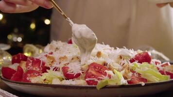 Chef, using spoon, adds white ranch dressing, made with garlic, sour cream, and mayonnaise, to delicious Caesar salad of vegetables, chicken, and croutons. video