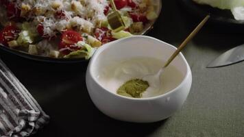 Cook adds small amount of powdered green seasoning, made from Italian herbs and marjoram, to plate that has white sauce, based on sour cream and mayo, that is specifically prepared for Caesar salad dressing. video