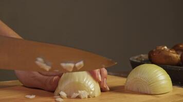 Chef deftly slices half of white onion into small pieces on wooden cutting board in the restaurant kitchen with a sharp knife. Close up. Slow motion video