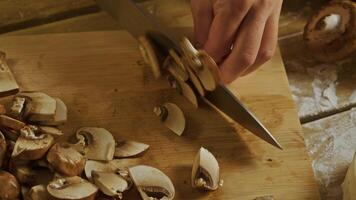 Cook cuts mushrooms into thin slices on a wooden chopping board, which is covered with flour, while preparing a vegetable stew. Top view video