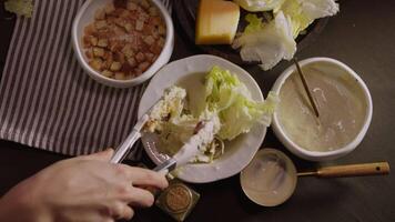 Home cooking. chef arranges iceberg lettuce leaves on plate. On table, there are ingredients for Caesar salad, as well as delicious white sour cream sauce. video