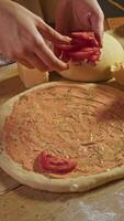 Establishment prepares traditional Italian pizza, featuring tomatoes, cheese, and sauce. chef meticulously arranges tomatoes on dough, adding unique touch to dish. Vertical. video