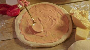 Female chef of restaurant is preparing pizza in kitchen. She spreads layer of uncooked pizza dough with mix of tomato sauce, garlic, and mayonnaise. top view video