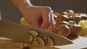 A brown mushroom is expertly sliced by the cook's skilled hands on a cutting board as part of the stew preparation. Close up. Slow motion video
