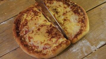 Delicious, freshly prepared pizza or khachapuri, with several types of cheese and tomatoes, is cut into quarters on the kitchen table with a knife. video