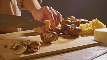 chef employs keen knife to precisely bisect brown mushroom, laying it on wooden cutting board. she dissect mushroom into thinner portions, ready for incorporation into dish featuring mushrooms. video