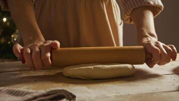 Housewife is kneading dough using rolling pin, rolling it in flour on wooden table in order to make festive pie. She is rolling out dough in order to give it round shape. video