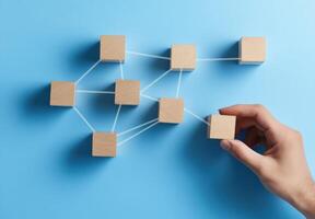 A hand connecting wooden blocks on a blue background, symbolizing networking, strategy, and teamwork in business. photo