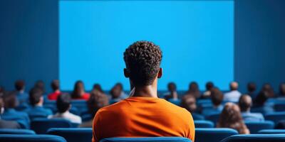 A diverse audience watches a presentation in a theater, focused on the blue screen ahead, highlighting engagement and curiosity. photo