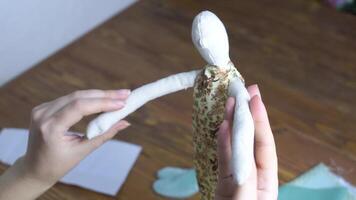 Human hands hold handmade rag toy. Doll in floral dress and many fabrics on wooden table. Diy handicraft concept. video