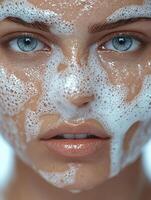 A close-up of a woman's face covered in cleansing foam, showcasing her clear blue eyes and smooth skin. photo