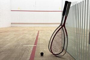 Two rackets and two squash balls lie on the parquet floor. Horizontal photo