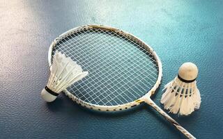 Cream white badminton shuttlecock and racket with neon light shading on dark floor in indoor badminton court, copy space, soft and selective focus. photo
