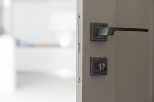 Chrome handle with keyhole on white door with panels in frames. Entrance. Close-up photo of architecture detail. Interior fragment as geometrical background with three rectangles and parallel lines