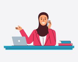 A smiling businesswoman in a hijab talks on her phone while gesturing towards a laptop on her desk vector