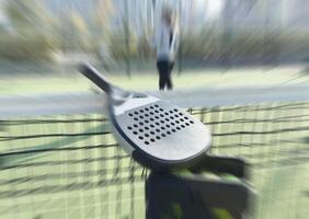 A padel or paddle tennis racket and a bright yellow tennis ball lie on a blue court. photo
