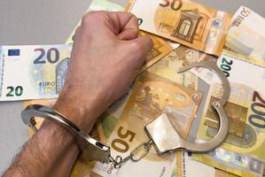 Folded hands and handcuffed hands resting on a table in front of money. photo