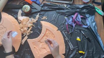 Hands cut hatchet form from foam polystyrene with blade on garbage bag. Craftsman's workshop. Woman makes viking axe for cosplay festival. Diy celtic weapon on wooden table. video
