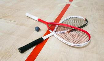 Two rackets and two squash balls lie on the parquet floor. photo