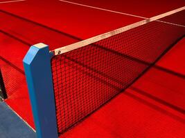 View of the net and the centre line of a red paddle tennis court. Racket sports photo