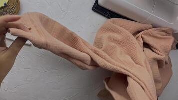 Needlewoman's hands checks the seams and appearance of new clothes made of cotton. Workshop of a fashion designer with sewing machine and white texture table. Craft and hobby. video