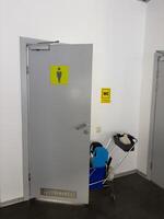 Door to men public toilet with cart for cleaning toilet service. Cleaning toilet in public place with help of cleaning trolley that serves wc, vertical photo