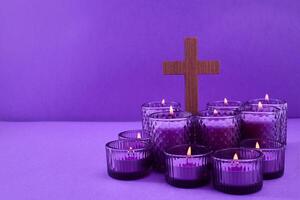 Lent Symbolism. Cluster of lit candles with a cross on a purple background. photo