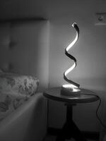 BW Photo of a spiral lamp standing on a table near the bed late in the evening,Modern design backdrop