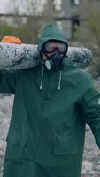 Worker in protective suit in radiation zone. Builder in safety uniform and gas mask is carrying pipe in destroyed place. Chemical attack. Vertical video