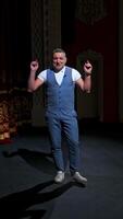 Man in front of empty theatre hall with red velvet chairs. Actor is standing on stage and talking with gestures before the performance. Vertical video