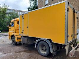 A big yellow car with a van is parked in the city yard. photo