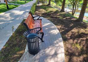 On a clear sunny spring day, there is a new urn and a brown bench in a shady park. photo
