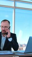 confiante o negócio pessoa falando a telefone dentro escritório. retrato do uma patrão sentado às mesa e lidando o negócio problemas através a telefone. vertical video