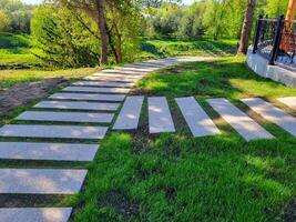 In the spring park, a path made of concrete rectangles is laid between the trees. The concept of landscaping and landscape design photo