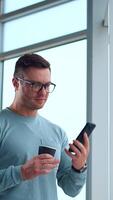 Relaxed businessman with a cup in his hand having lunch break. Man is looking at phone taking or having conversation. Vertical video