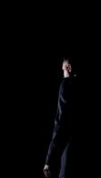 Speaker on black background. Profile view of a man talking to the audience while standing on stage. Performer in darkness. Vertical video