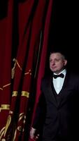 Portrait of a host. Man actor in black costume appears on stage and begins the speech in bright light spot in the theater. Vertical video