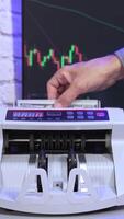 Modern counter machine on large monitor background. Man's hand putting paper money into a counting machine and takes them after financial operation. Vertical video