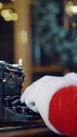 Santa Claus is sitting at the table and typing a letter of congratulations for the New Year on the typewriter in the room on a blurred background. Close-up Vertical video
